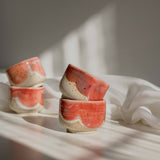 Stacks of handcrafted espresso cups in coral red finish, illuminated by contrasting light and shadows.