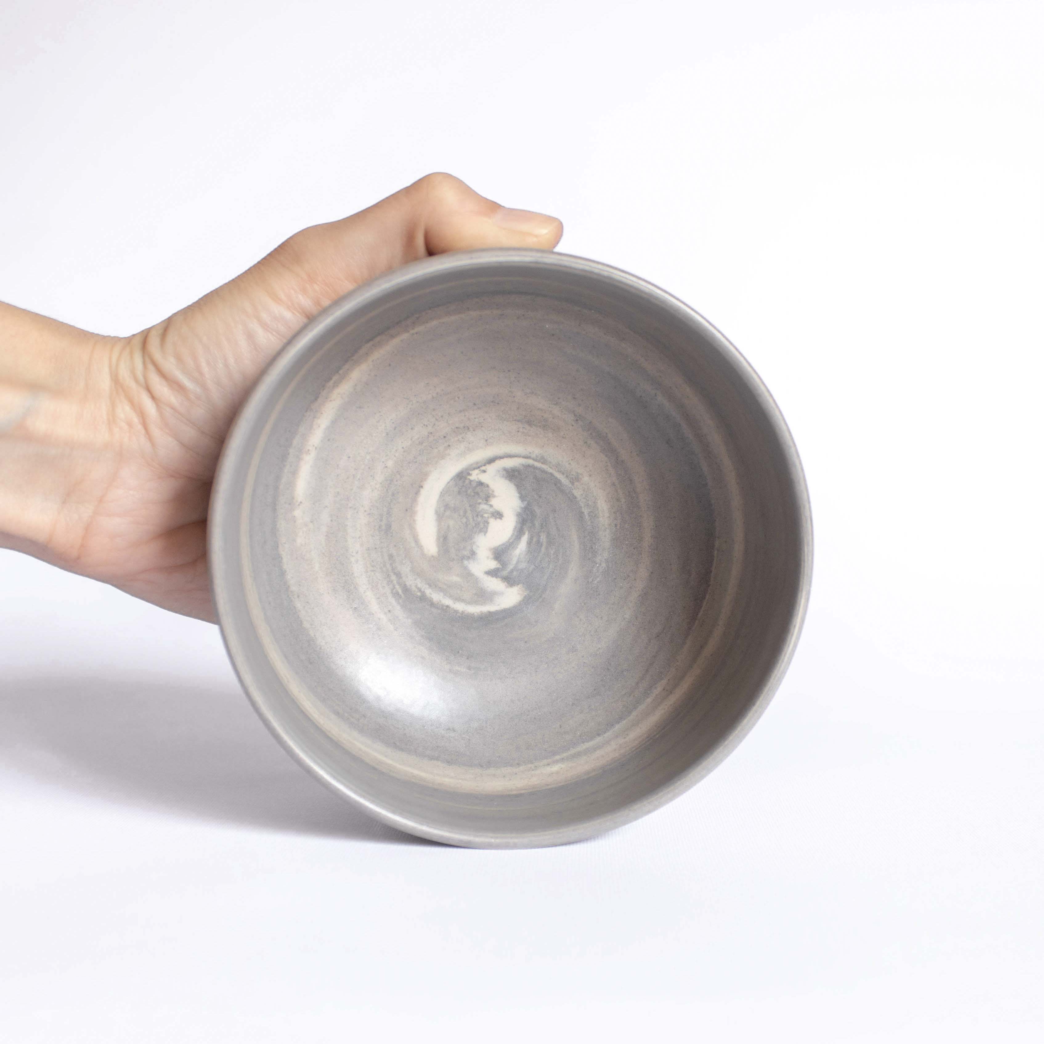 Close-up of a handmade ceramic bowl's interior in earthy, natural tones, held against a white backdrop