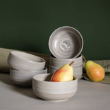 Elegant table setup featuring handmade ceramic bowls in earthy tones, accompanied by fresh pears and draped fabric.