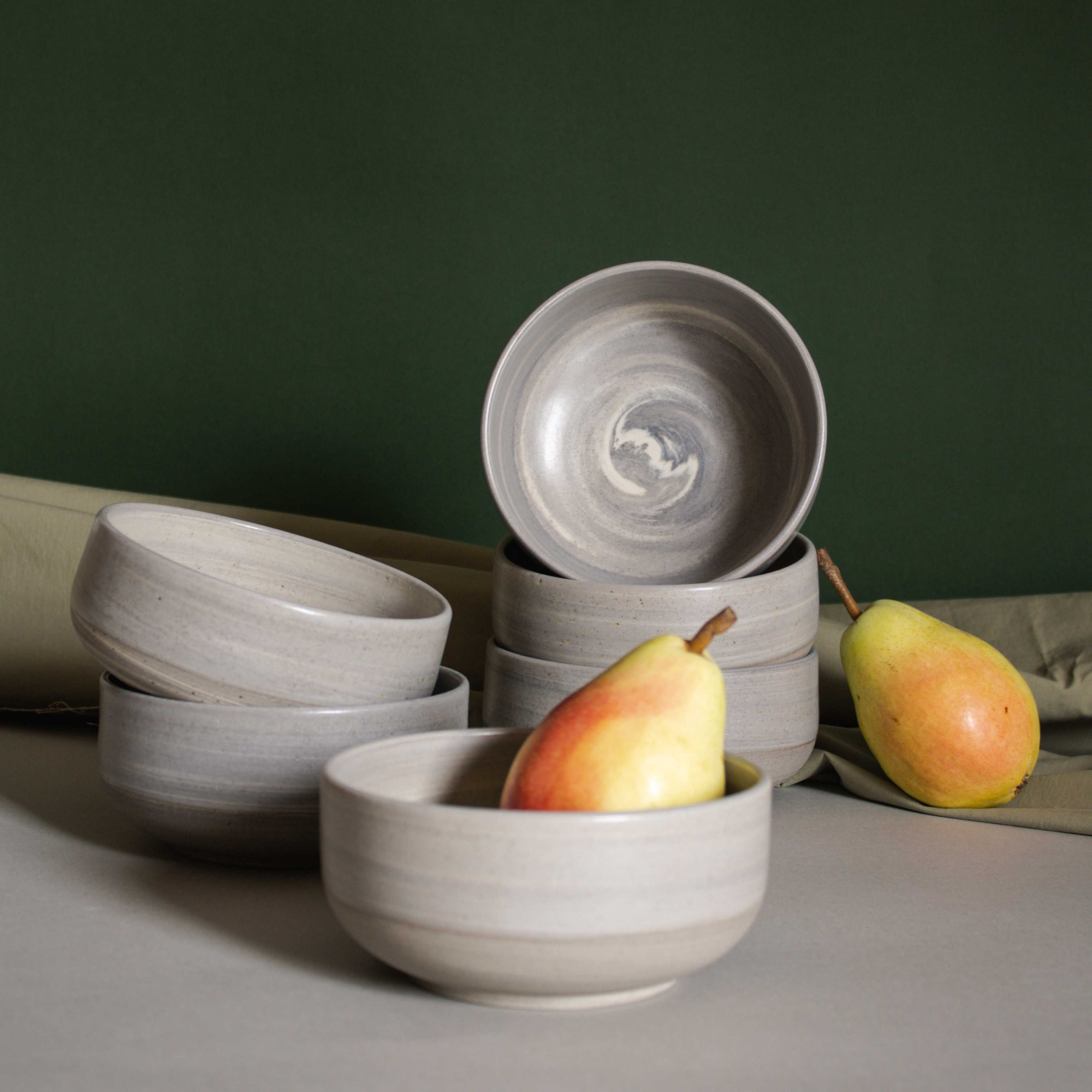 Elegant table setup featuring handmade ceramic bowls in earthy tones, accompanied by fresh pears and draped fabric.