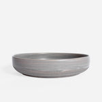 Handcrafted ceramic pasta plate with a matte earthy finish, displayed on a white background.