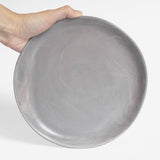 A handmade ceramic plate in gray with a satin matte finish, held against a white background.