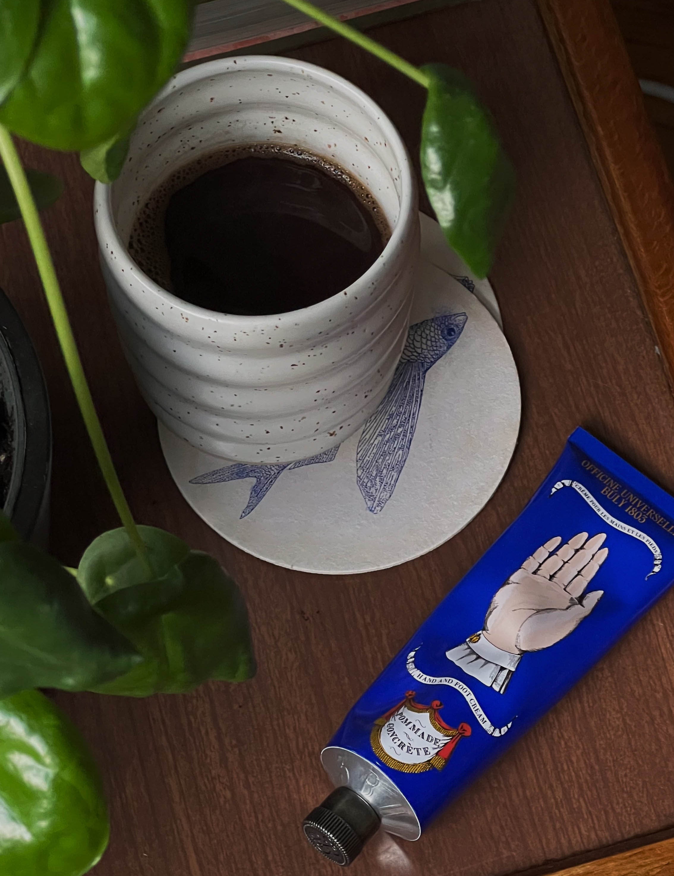 Black coffee served in a handmade ceramic Ripple Speckled White cup by Made of Dust Ceramics, on a wooden table surrounded by house plants.