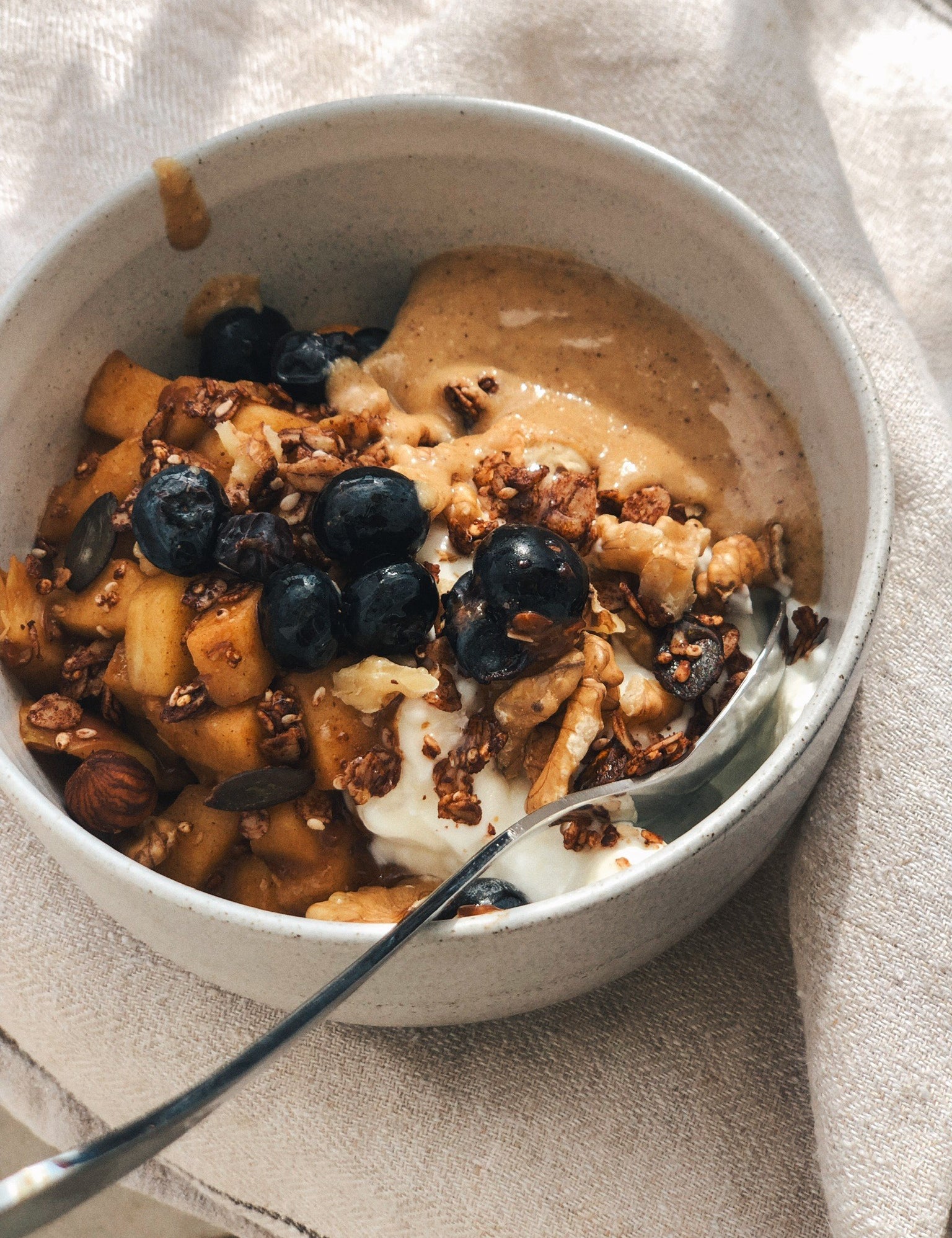 Granola with blueberries served in a handmade ceramic bowl on a linen tablecloth.