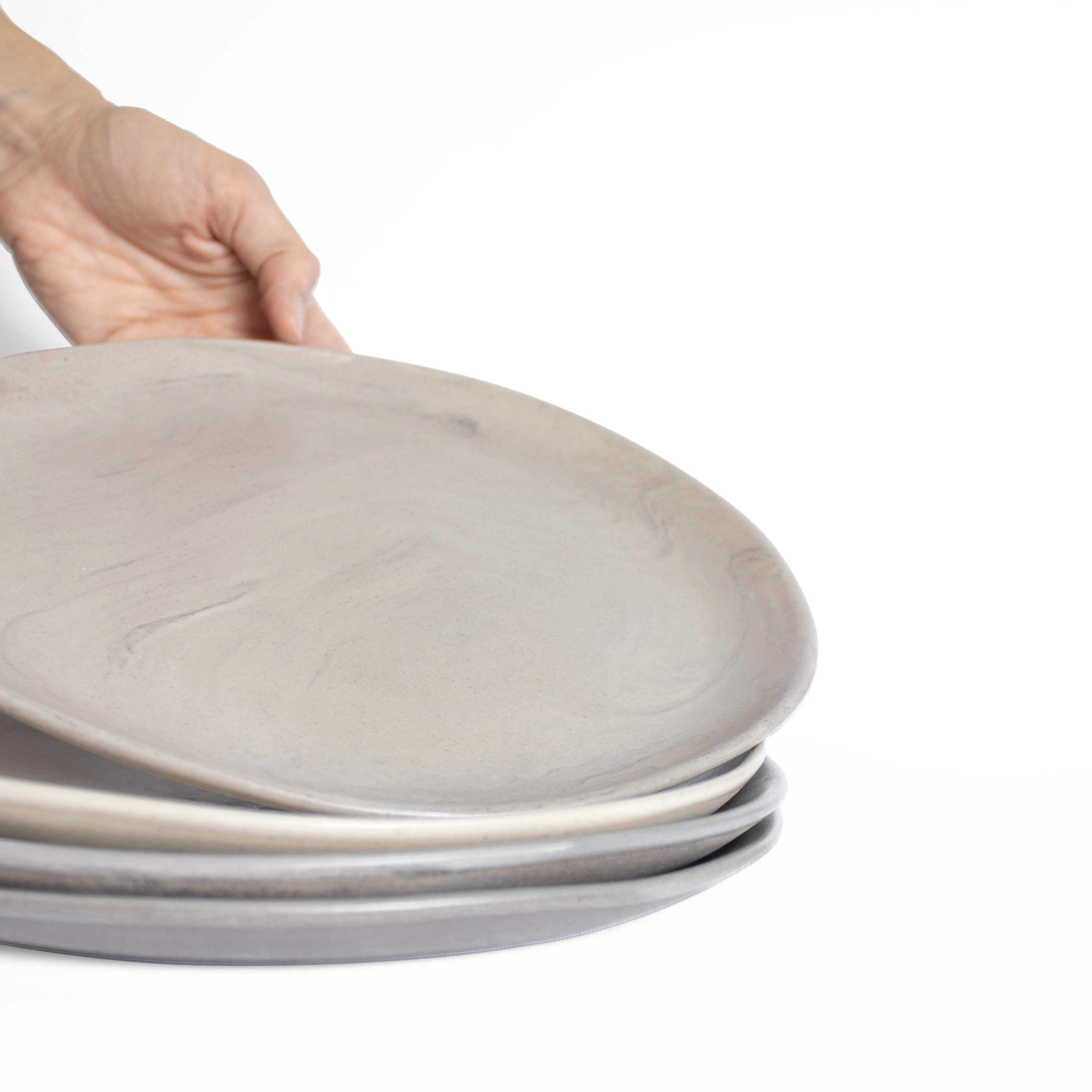 A stack of artisanal ceramic plates in natural earthy tones displayed against a white background.