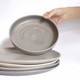 Handcrafted pasta plate with an earthy finish, held against a stack of handmade lunch plates, placed against a white background.