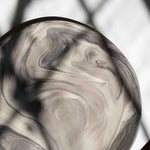 A handcrafted marbled ceramic plate featuring gray and beige tones, illuminated by a striking beam of light.