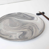 A handcrafted marbled ceramic plate and chopsticks arranged neatly on a white surface.