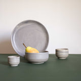 A collection of handcrafted marbled ceramic pieces in natural earthy tones arranged on a dark green surface.