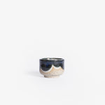 Handmade ceramic espresso cup crafted from speckled cream clay, adorned with an organic deep blue and white glaze pattern, captured against a white backdrop.