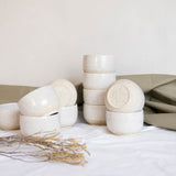 Speckled white ceramic cappuccino cups displayed with pale green and white cloth, alongside branches.