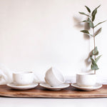 Handmade speckled white ceramic cappuccino cups with saucers arranged on a rustic wooden board.