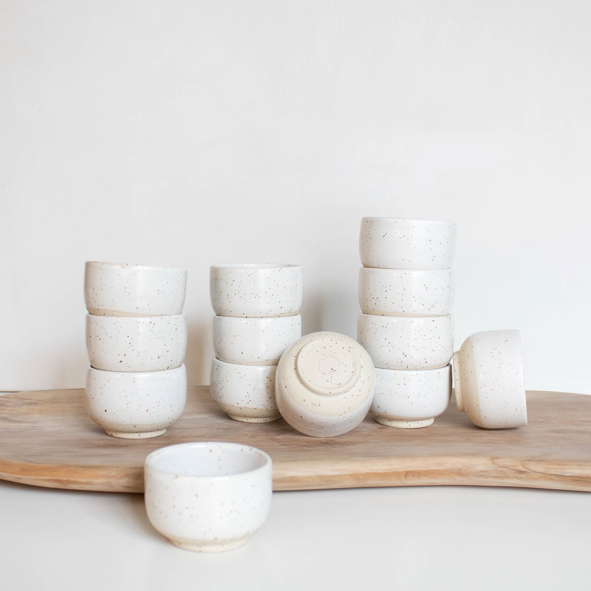 Handmade speckled white ceramic espresso cups arranged on a rustic wooden board.