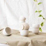 Speckled white ceramic espresso cups showcased with a house plant on a pastel green cloth.