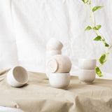 Speckled white ceramic espresso cups showcased with a house plant on a pastel green cloth.