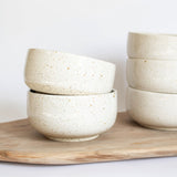 Handcrafted ceramic bowls in speckled white finish arranged on a rustic wooden board.