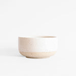 A handcrafted ceramic bowl in speckled white finish, set on a white background.