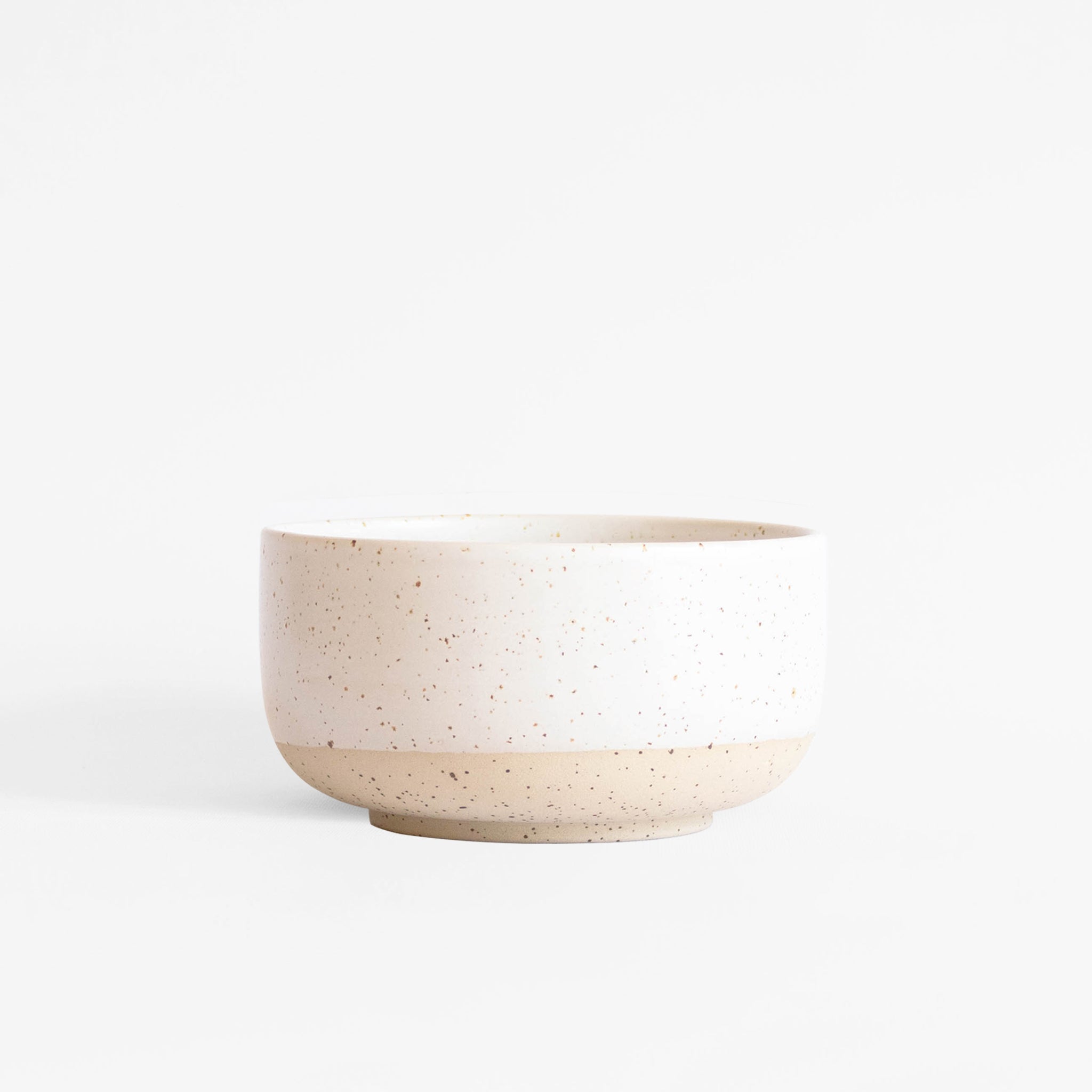 A handcrafted ceramic bowl in speckled white finish, set on a white background.