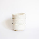 Stack of handcrafted bowls in speckled white finish, showcased in front of a white backdrop.