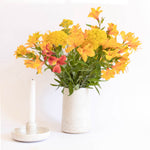 A handcrafted ceramic vase in speckled white finish, holding a bouquet of yellow flowers, set on a white background.