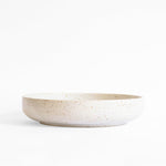 A handmade ceramic plate in speckled white finish, set against a white background.