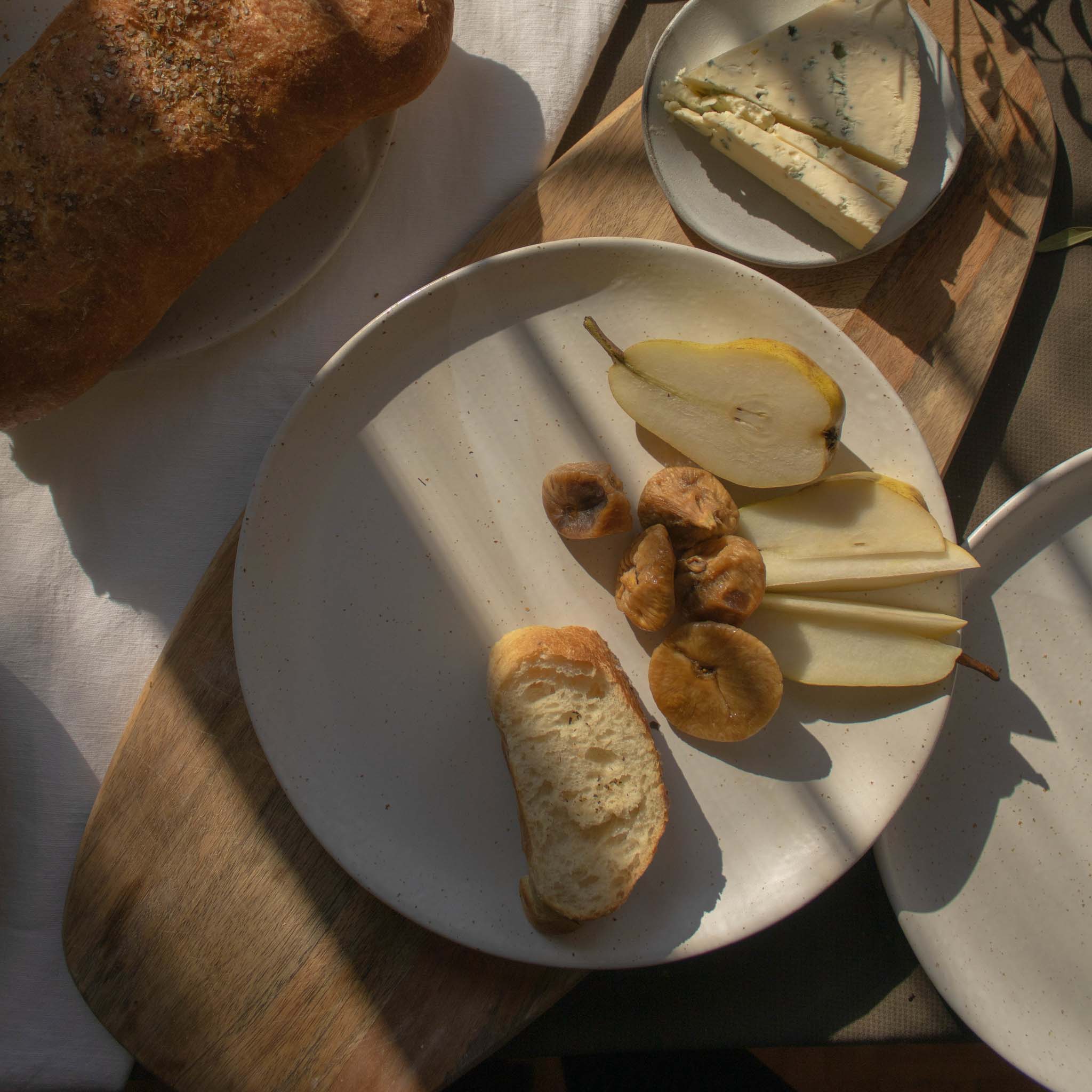 Handmade ceramic plate in speckled white finish, displayed with a selection of appetizers including olives, cheese, bread, and pears.