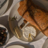 Handmade ceramic plate in speckled white finish, displayed with a selection of appetizers including olives, cheese, bread, and pears.