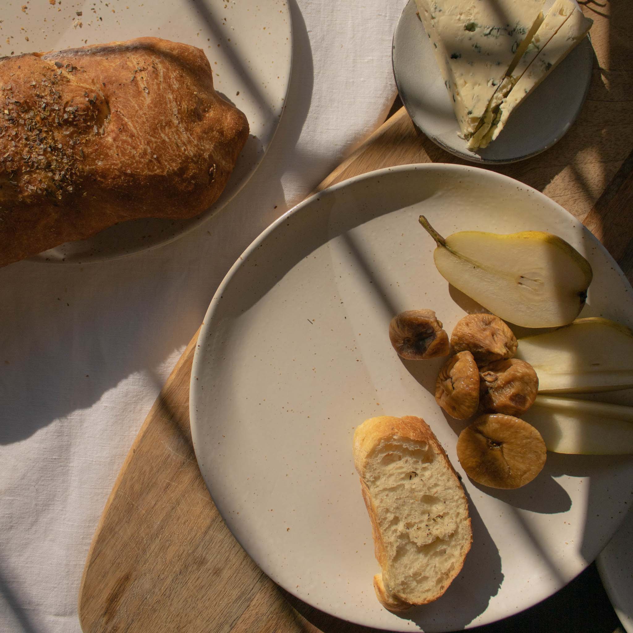 Handmade ceramic plate in speckled white finish, displayed with a selection of appetizers including olives, cheese, bread, and pears.