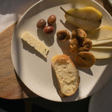 Handmade ceramic plate in speckled white finish, displayed with a selection of appetizers including olives, cheese, bread, and pears.