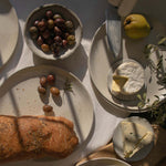 Overhead view of handmade ceramic plates in speckled white finish, displayed with a selection of appetizers.
.