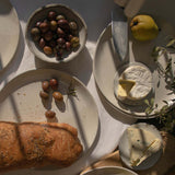 Overhead view of handmade ceramic plates in speckled white finish, displayed with a selection of appetizers.
.