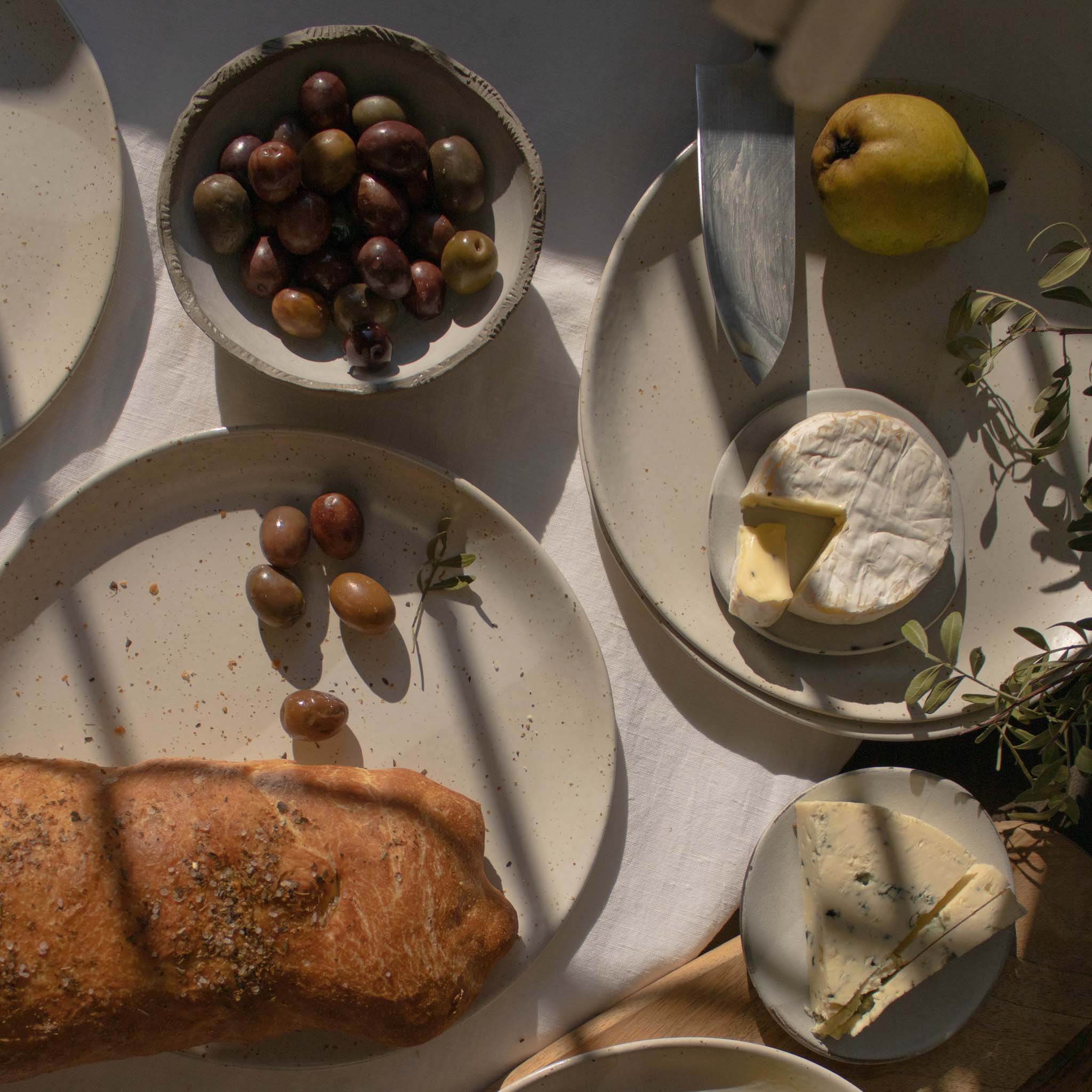 Overhead view of handmade ceramic plates in speckled white finish, displayed with a selection of appetizers.
.