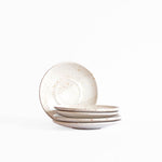 A stack of handcrafted ceramic saucer plates in speckled white finish, displayed on a white background.