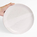 A handmade ceramic plate in speckled white finish, held against a white background.