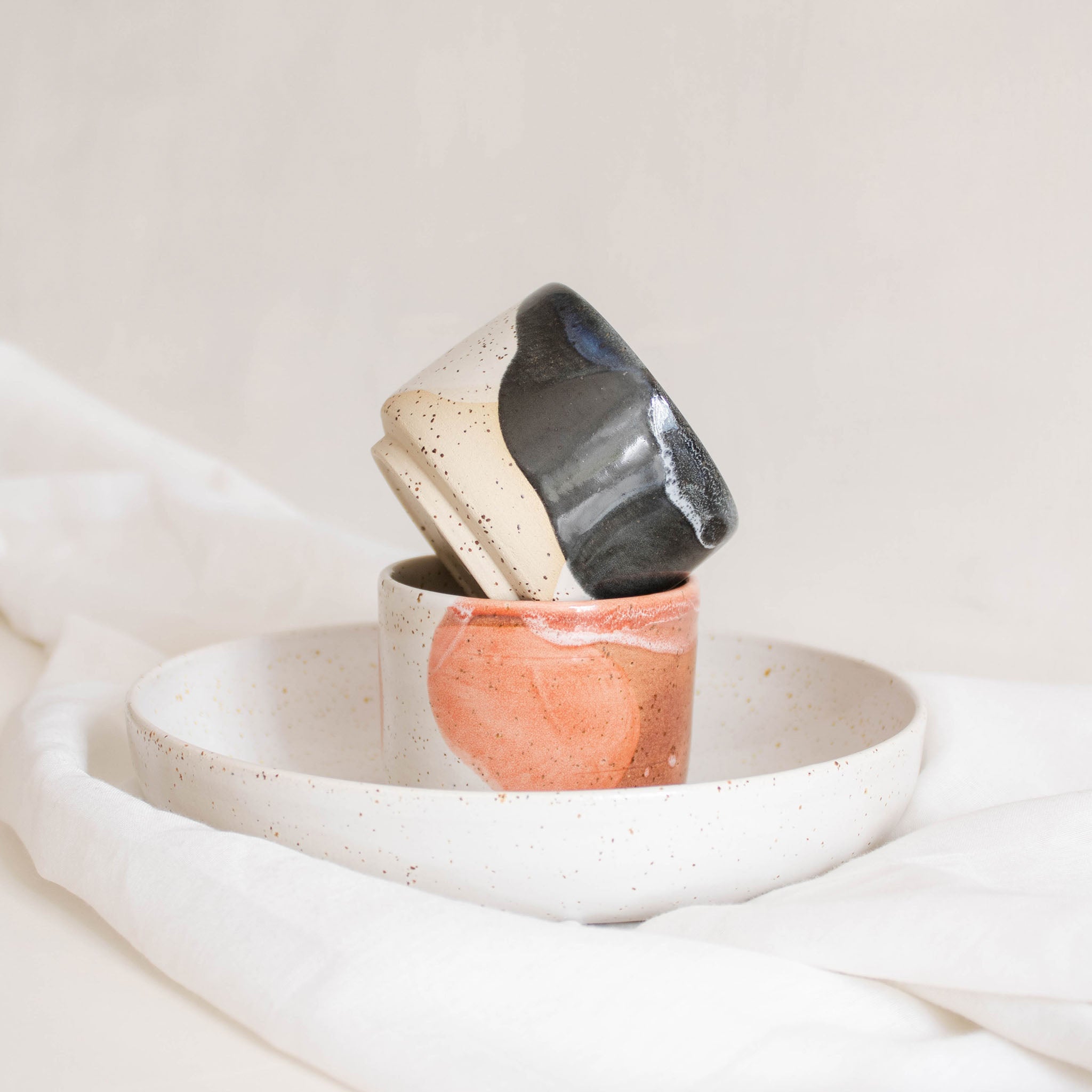 Handcrafted ceramic cups in deep blue and pink set on a speckled white pasta plate.