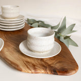 Handmade speckled white ceramic cappuccino cup with saucer plate on wooden board.