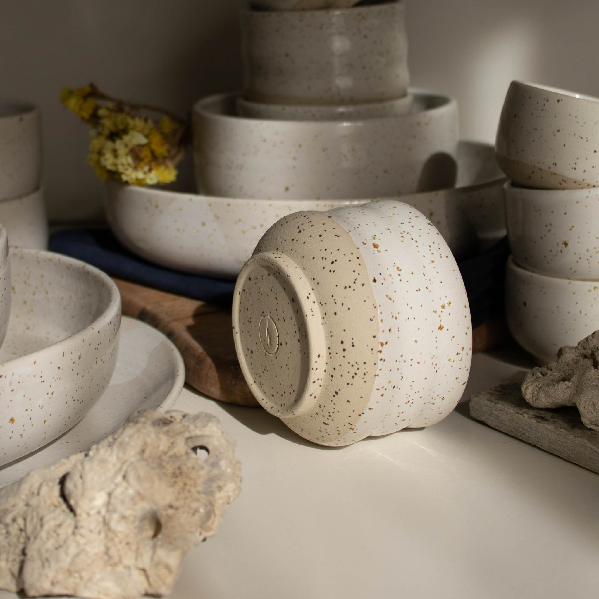 Handmade ceramic cup in speckled white finish, in a beam of light.