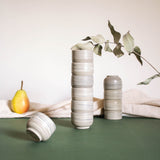 Stacks of espresso cups with a matte marble finish in natural earthy tones, displayed alongside draped fabric and fruits.