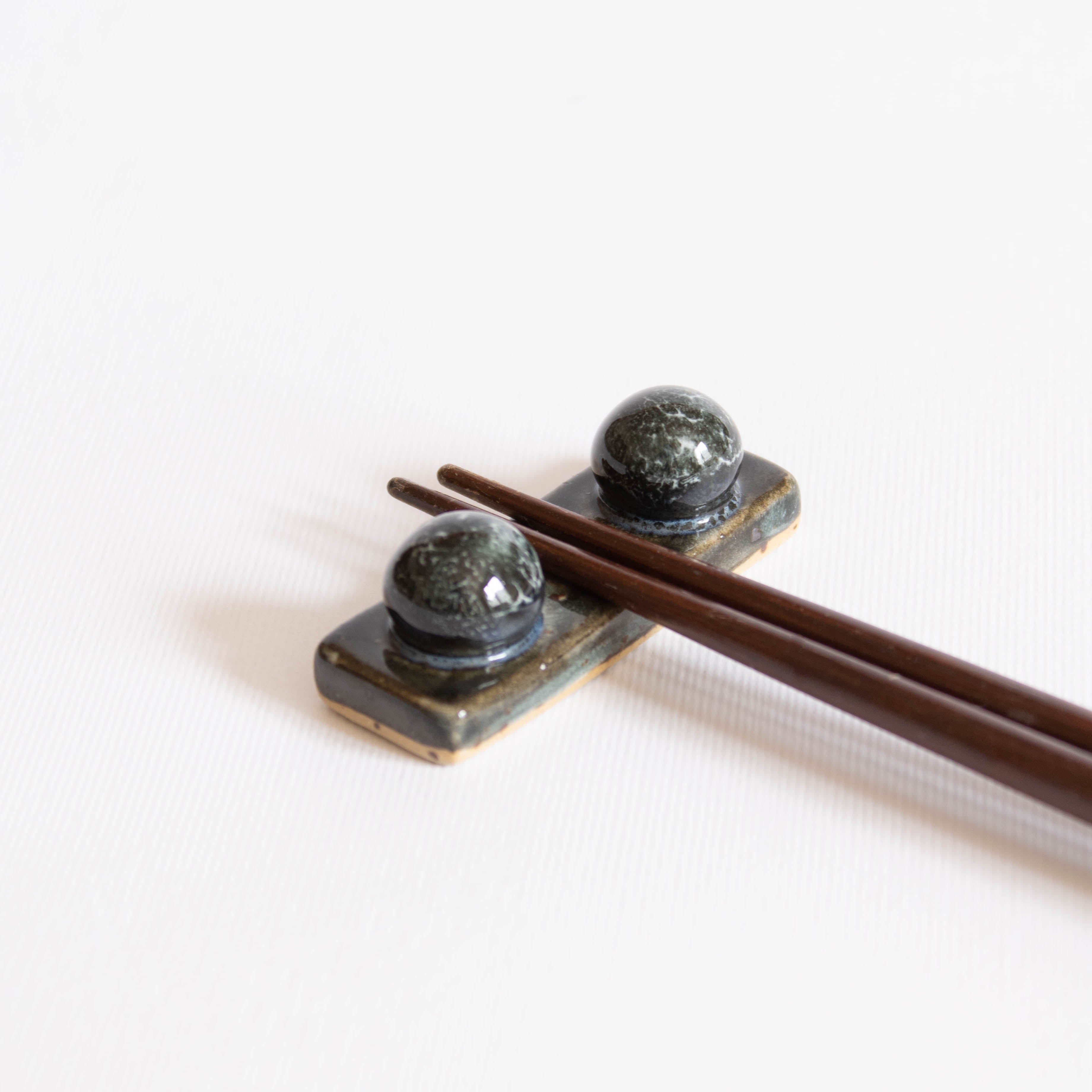 Handcrafted midnight blue chopstick rest with wooden chopsticks displayed on a white surface.