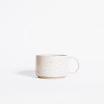 A handcrafted ceramic mug in speckled white finish, set on a white background.