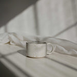 A handcrafted ceramic mug in speckled white finish, illuminated by a beam of light.