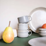 An arrangement of artisanal ceramic cups with handles, featuring natural earthy tones, neatly stacked on a tabletop.