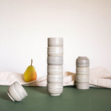 Stacks of espresso cups with a matte marble finish in natural earthy tones, displayed alongside draped fabric and fruits.