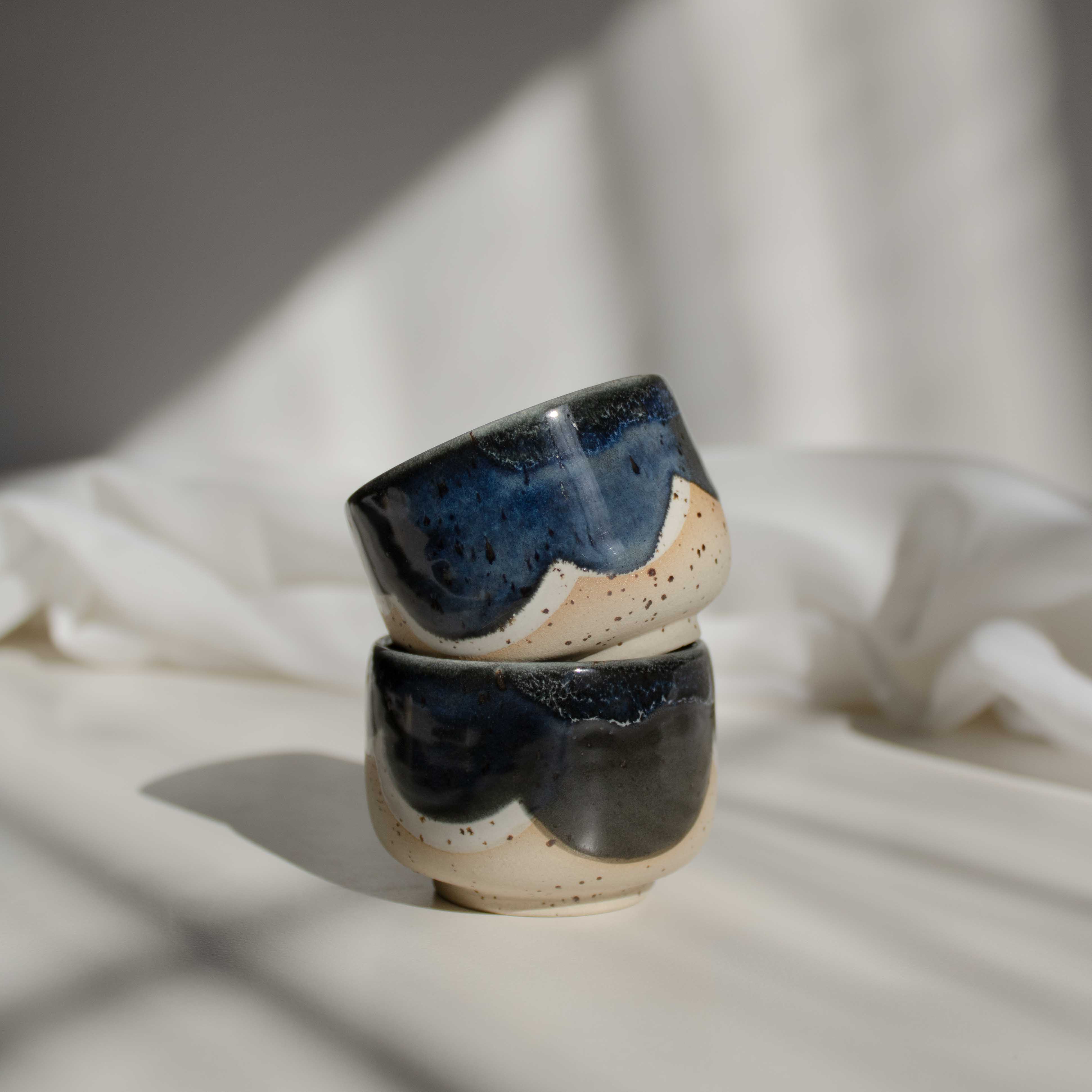 Stacks of handcrafted espresso cups in deep blue finish, illuminated by contrasting light and shadows.