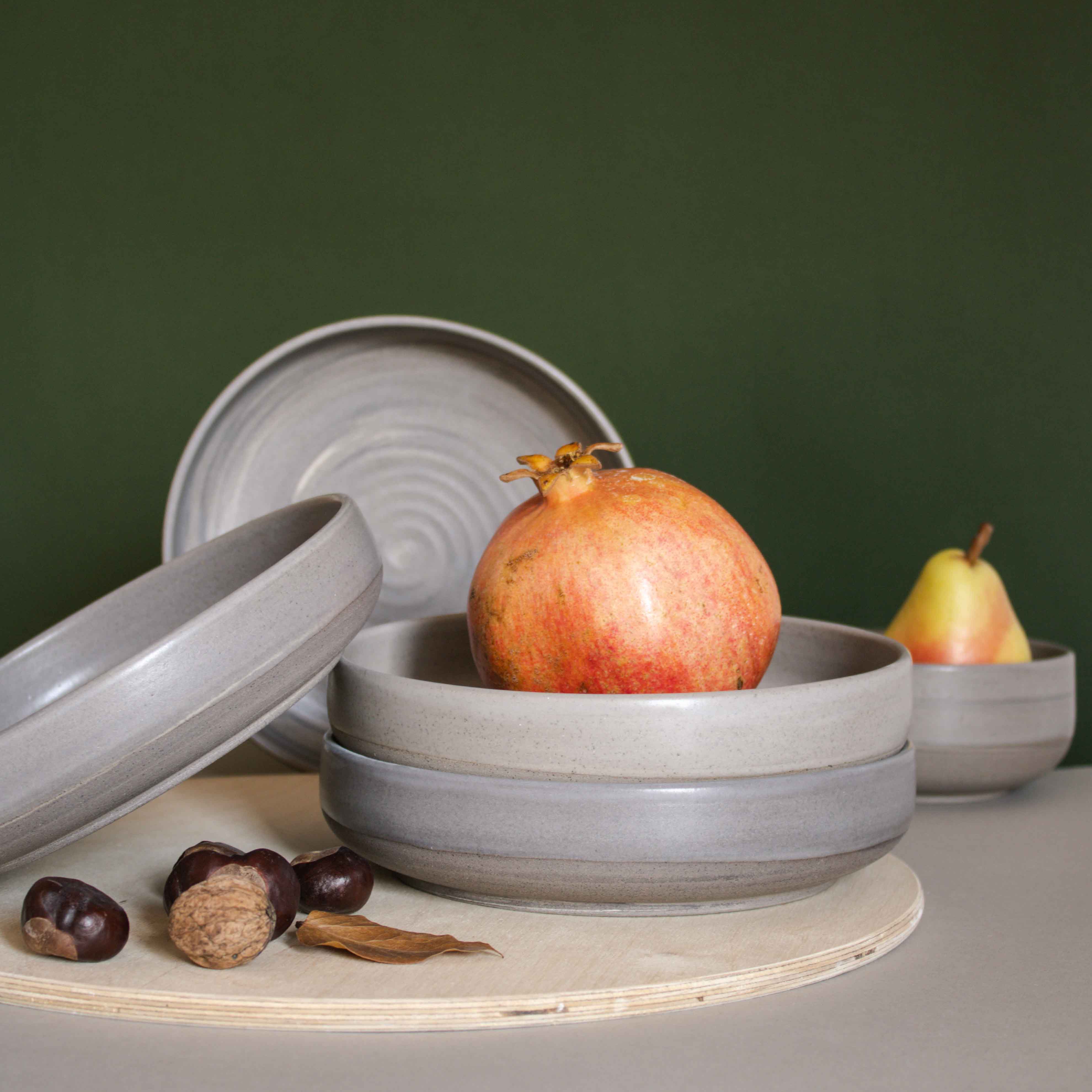 Table arrangement featuring handmade ceramic pasta plates in a matte earthy finish, complemented by walnuts and fruits.