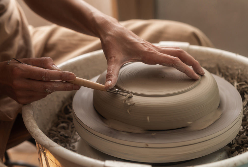 Hands using a pottery trimming tool to refine the base of a ceramic plate.