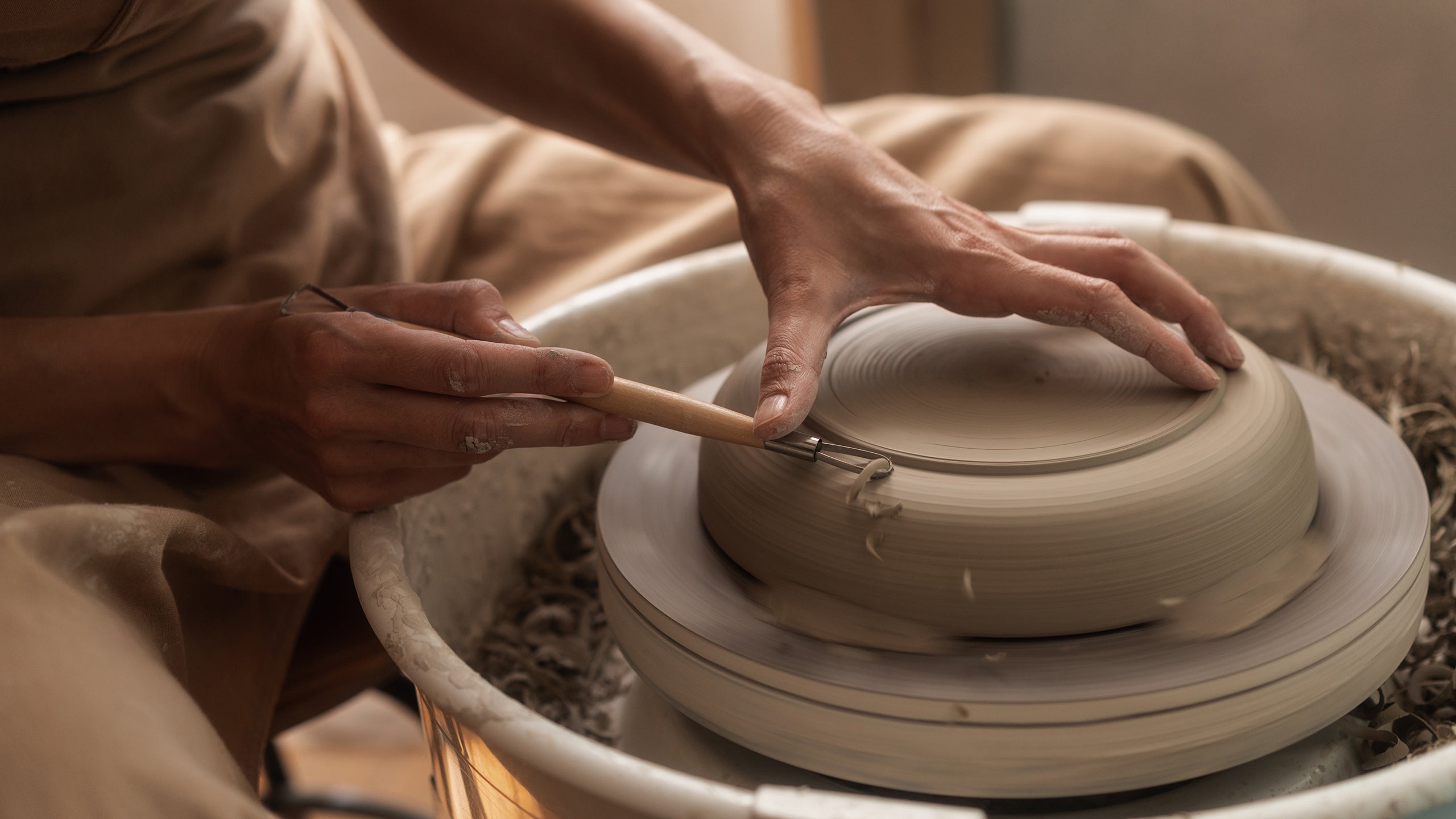 A potter at a pottery studio trims a ceramic plate on a wheel.