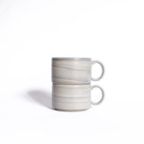 Two meticulously crafted ceramic cups with handles, stacked neatly against a clean white background.