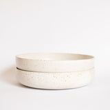 Two handcrafted ceramic pasta plates in speckled white finish, displayed on a white background.